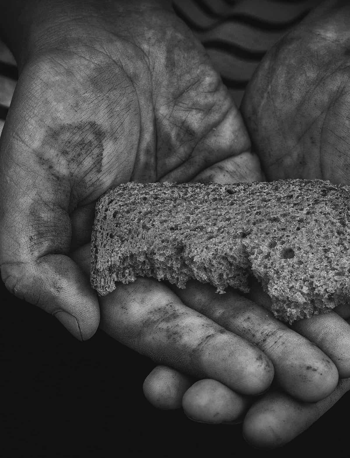 Zwei Hände halten ein angebissenes Brot, schwarz-weiß